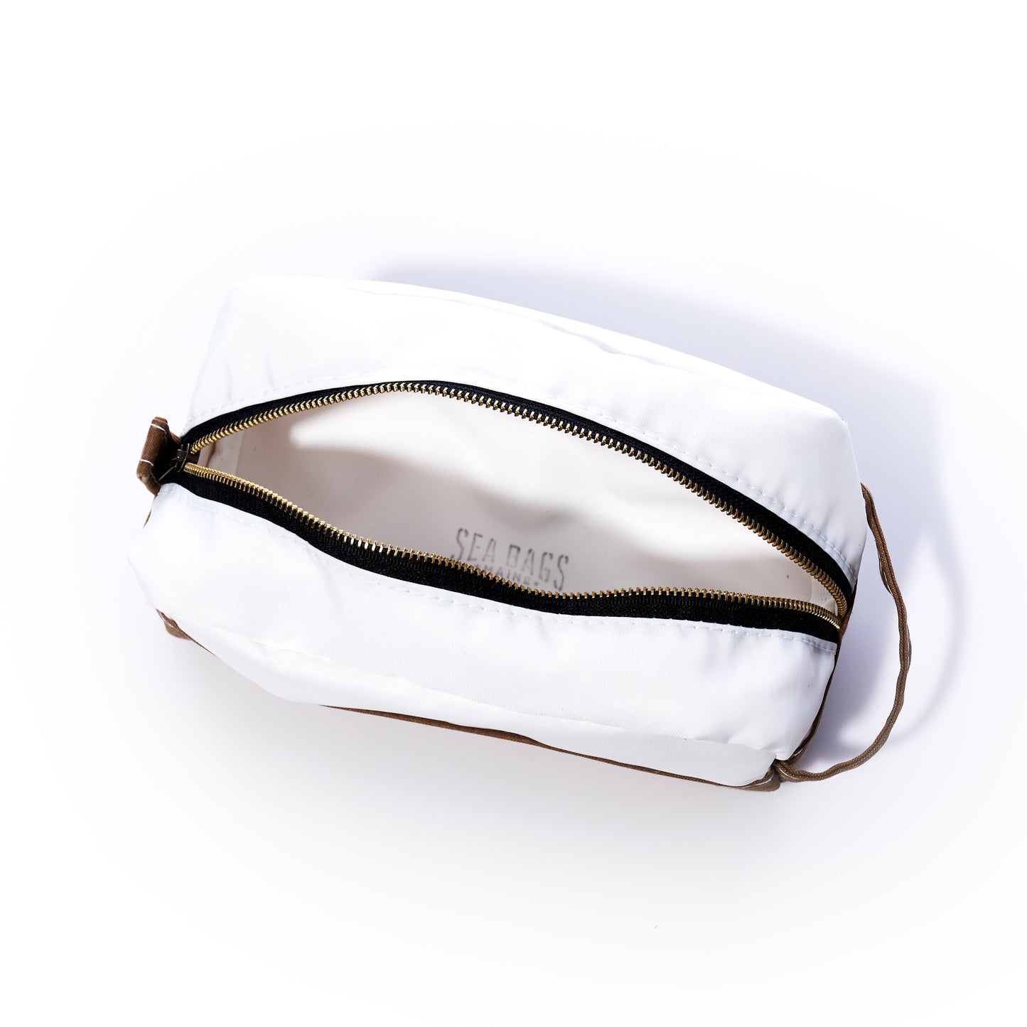 The Sea Bags Tan Chebeague Toiletry Bag is a rectangular white zippered pouch crafted from durable Dacron sailcloth, featuring a brown strap. Shown partially unzipped to display the interior, it is set against a white background. by Sea Bags