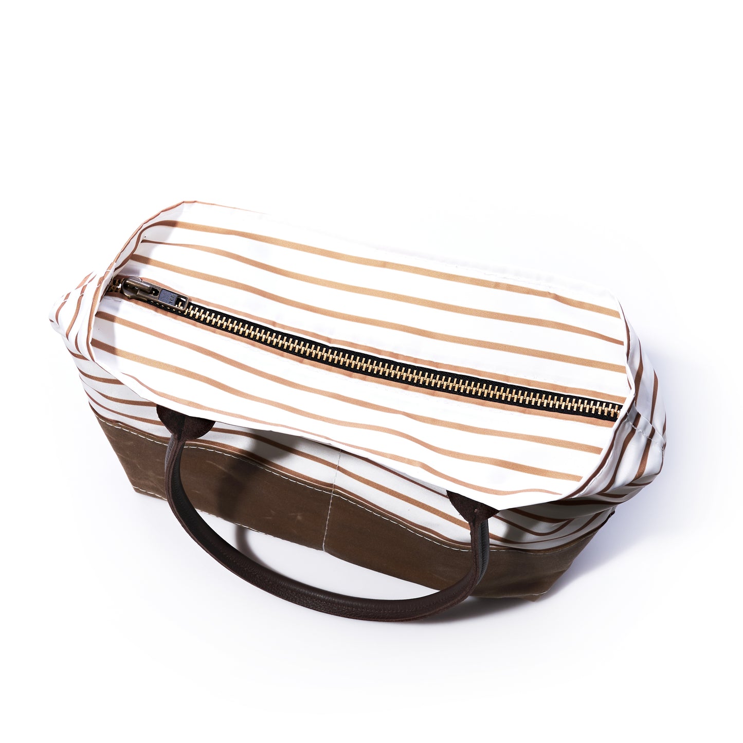 Top view of the Sea Bags Tan Chebeague Stripe Handbag, featuring a striped fabric design with brown handles and a visible gold zipper. Inspired by the charm of Chebeague Island, this bag displays horizontal tan and white stripes on the upper section, evoking timeless maritime style. by Sea Bags