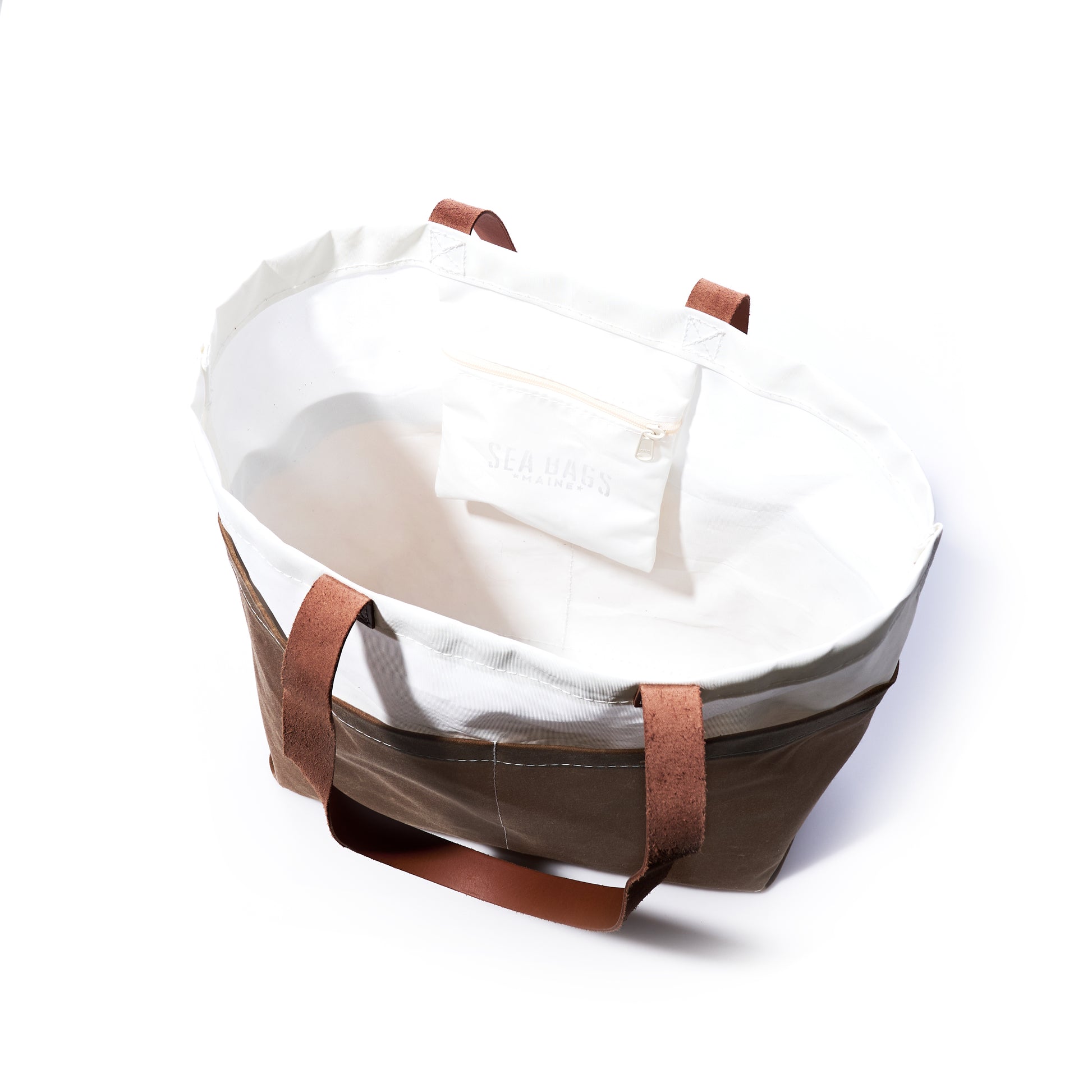 The Tan Chebeague Market Tote by Sea Bags is a large, open-top tote crafted from durable waxed canvas, featuring brown handles and trim, a white interior, and a small zippered pocket inside. by Sea Bags