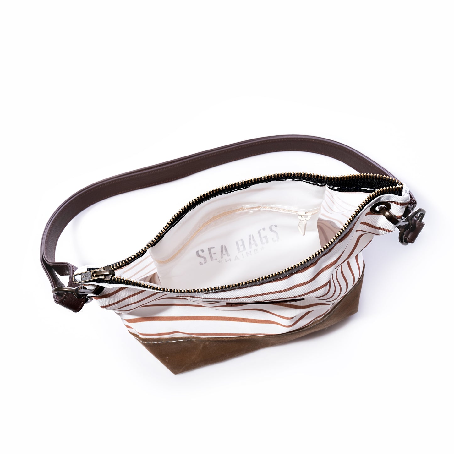 The Tan Chebeague Stripe Crossbody by Sea Bags is shown open, featuring brown and white stripes with a dark leather shoulder strap. Its white interior is labeled Sea Bags. Made from recycled sailcloth, the empty bag is displayed on a white background. by Sea Bags