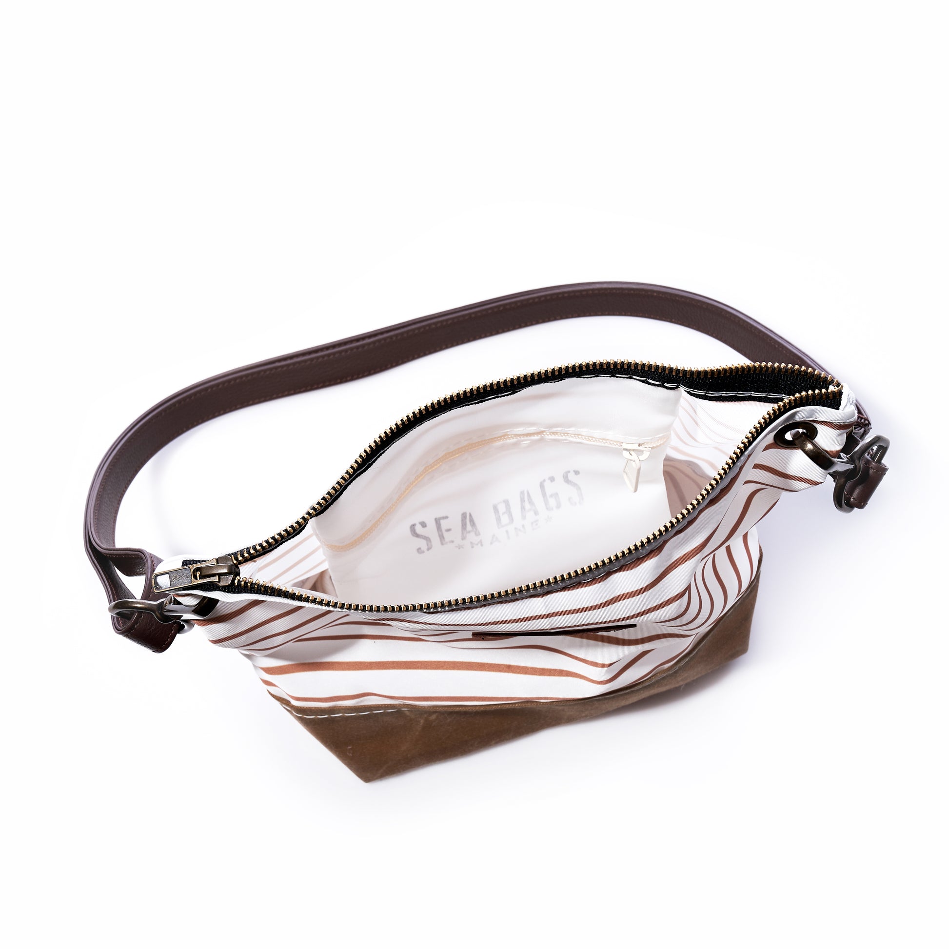 The Tan Chebeague Stripe Crossbody by Sea Bags is shown open, featuring brown and white stripes with a dark leather shoulder strap. Its white interior is labeled Sea Bags. Made from recycled sailcloth, the empty bag is displayed on a white background. by Sea Bags