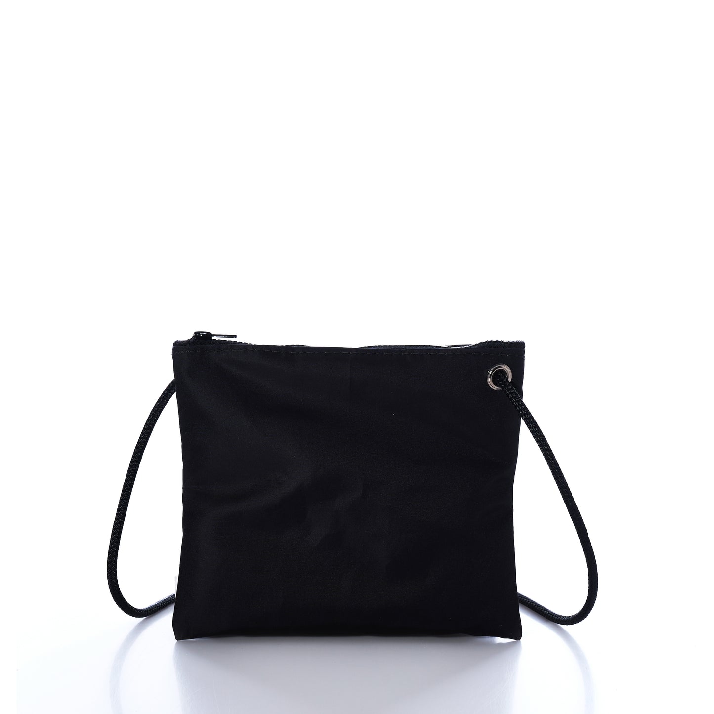 The Jolly Roger Slim Crossbody by Sea Bags is a small black zippered pouch made from durable sailcloth, featuring a thin black strap. It is displayed upright against a white background with a reflective surface. by Sea Bags