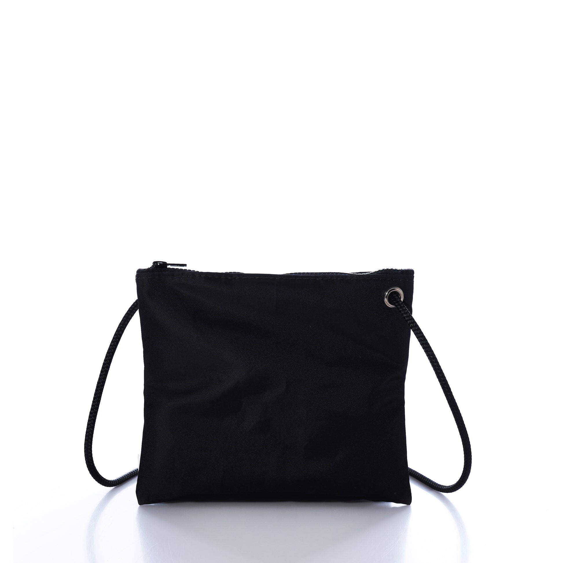 The Jolly Roger Slim Crossbody by Sea Bags is a small black zippered pouch made from durable sailcloth, featuring a thin black strap. It is displayed upright against a white background with a reflective surface. by Sea Bags