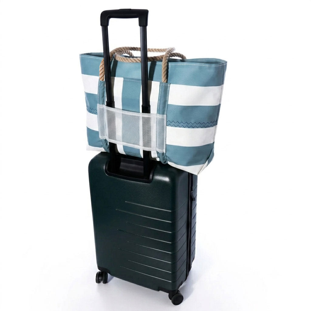 A blue and white striped tote bag with rope handles and a clear mesh side pocket, shown attached to a dark green rolling suitcase on a white background.