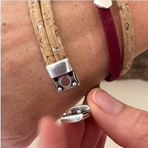 A hand fastens the Elisabetta Studio Classic Cork Bracelet Clover on Olive, crafted in Vermont from natural and magenta cork strips and secured with a silver magnetic clasp. by Sea Bags
