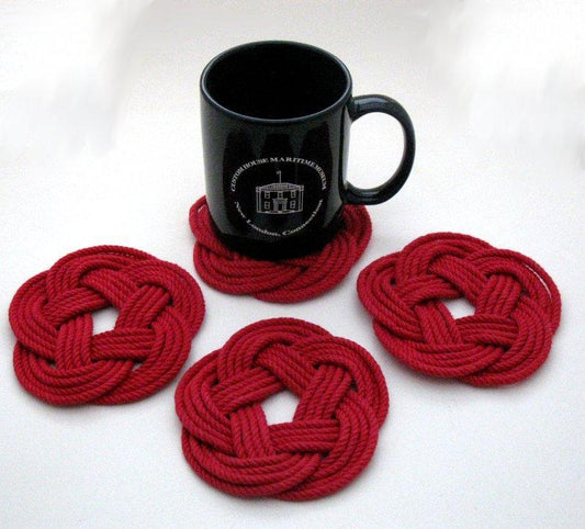 A black mug rests on one of the true Nautical Sailor Knot Coasters Set of 4 in red, arranged on a white background.