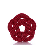 The true Nautical Sailor Knot Trivet - Red features a handwoven cotton rope, tied into an elaborate flat Turk’s head knot, reminiscent of classic nautical décor and set against a white background. by Sea Bags