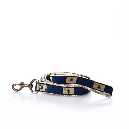 Introducing the Maine Flag Dog Leash by Belted Cow—a coiled blue fabric, heavy-duty leash with a brass clip and a distinctive pattern of trees on tan rectangles along its length. Perfect for adventurous pups.