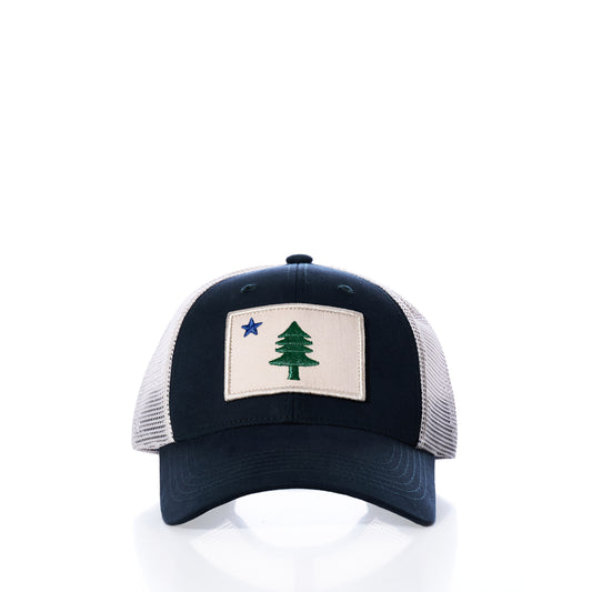 The Maine Flag Trucker Hat by true features a navy blue and white mesh design with a front patch depicting a green tree and blue star on a beige background, offering classic New England style inspired by the iconic Maine state flag.