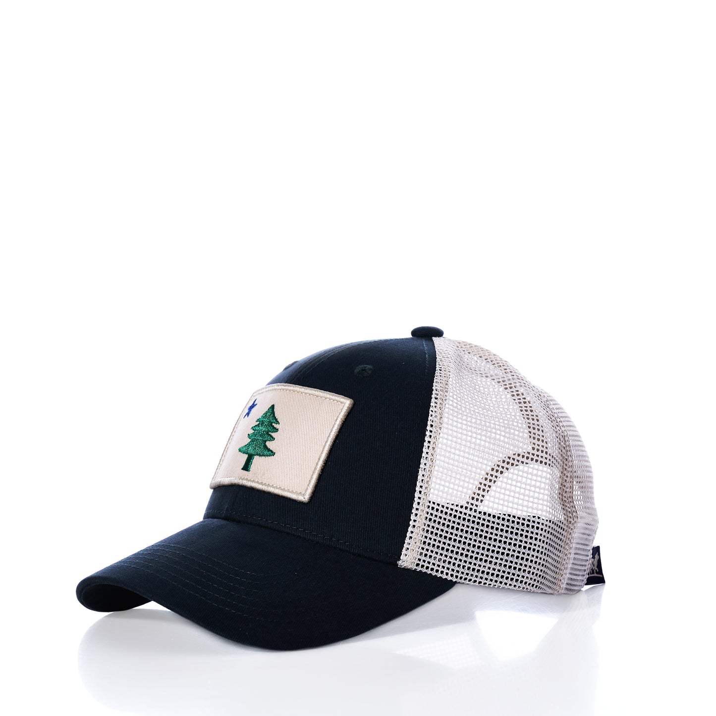 The Maine Flag Trucker Hat by true is a black and white mesh trucker hat with a beige patch featuring a green tree emblem on the front, displayed on a white background.