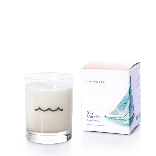 The Smooth Sailing Eco-Friendly Candle by Shore Soap Co. rests beside its box, adorned with a sailboat illustration and the brand’s signature design. Made from glass and eco-friendly soy wax with phthalate-free fragrance, this candle is presented in a reusable keepsake tumbler—perfect for enjoying long after the scent has faded.