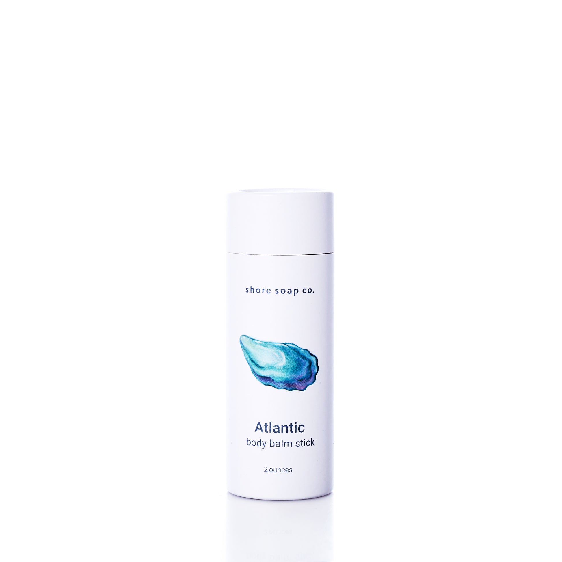 A white tube labeled “Atlantic Eco-Friendly Body Balm Stick” by Shore Soap Co., featuring a blue shell illustration on the front and containing 2 ounces, is centered on a white background. This concentrated moisturizer provides hydration for dry skin while serving as an eco-friendly body balm choice.