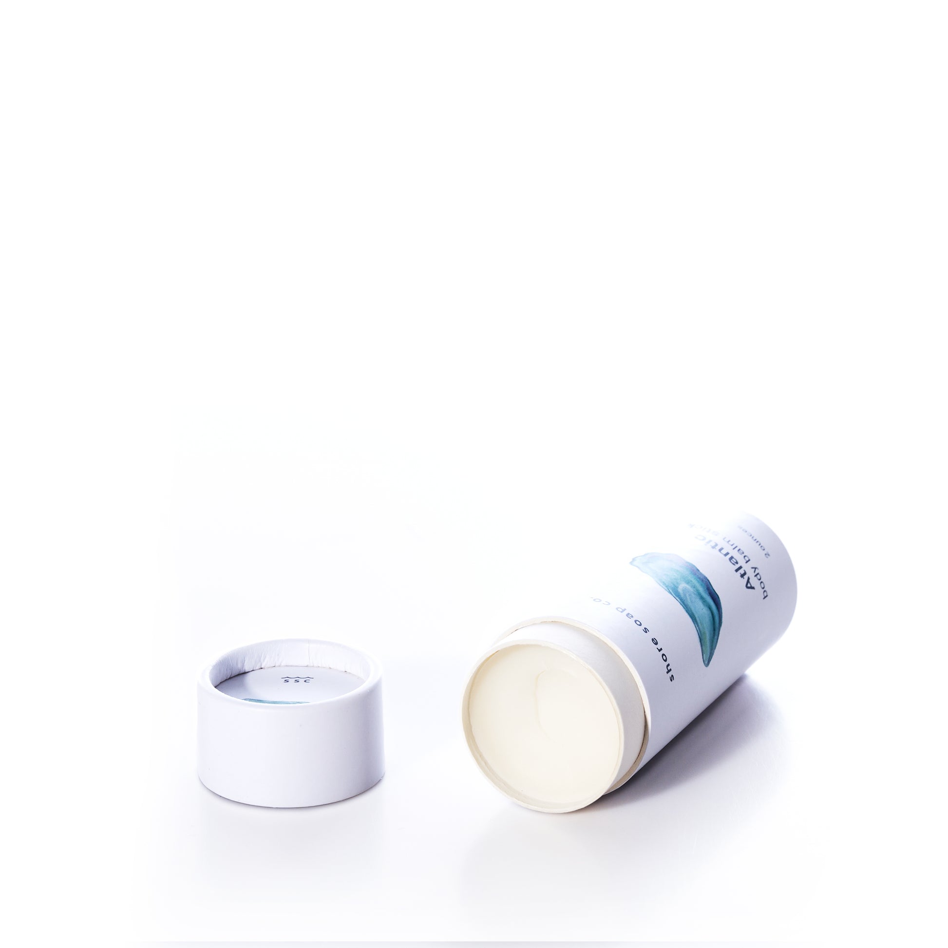 A white cylindrical container of true’s Atlantic Eco-Friendly Body Balm Stick lies on its side with the lid removed, revealing a concentrated moisturizer inside—perfect for hydrating dry skin—all against a white background.