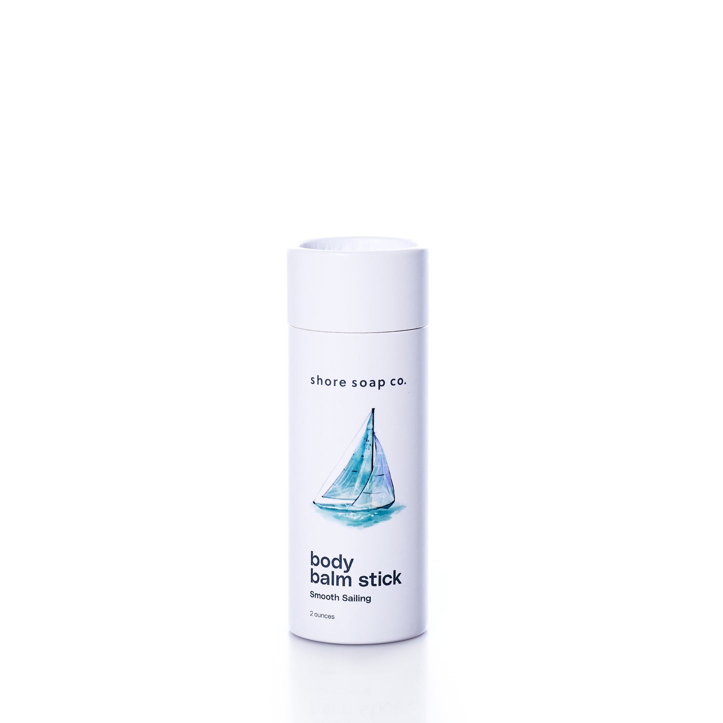 A white cylindrical container labeled “Shore Soap Co. Smooth Sailing Eco-Friendly Body Balm Stick,” featuring a sailboat illustration on the front, sits against a white background. This pocket-sized balm offers instant, eco-friendly hydration for dry skin whenever you need on-the-go relief.