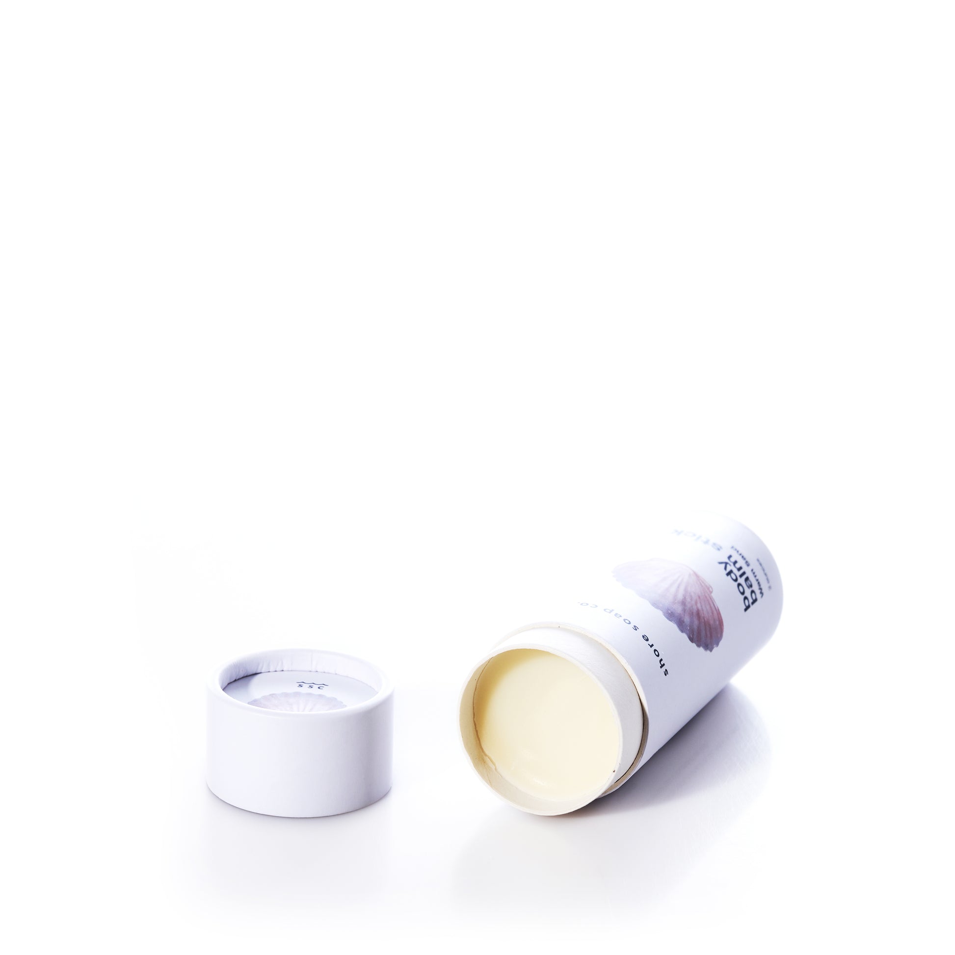 A cylindrical container with a removed lid displays the Shore Soap Co Warm Sand Eco-Friendly Body Balm Stick—a solid cream product designed as a concentrated moisturizer for intense hydration—set against a white background.
