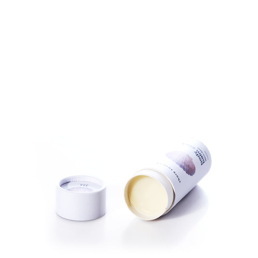 A cylindrical container with a removed lid displays the Shore Soap Co Warm Sand Eco-Friendly Body Balm Stick—a solid cream product designed as a concentrated moisturizer for intense hydration—set against a white background.