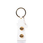 A White Lighthouse Door Chime keychain from true, featuring a gold keyring and two gold dials on the front, reminiscent of a New England Bells lighthouse door chime, photographed against a white background.