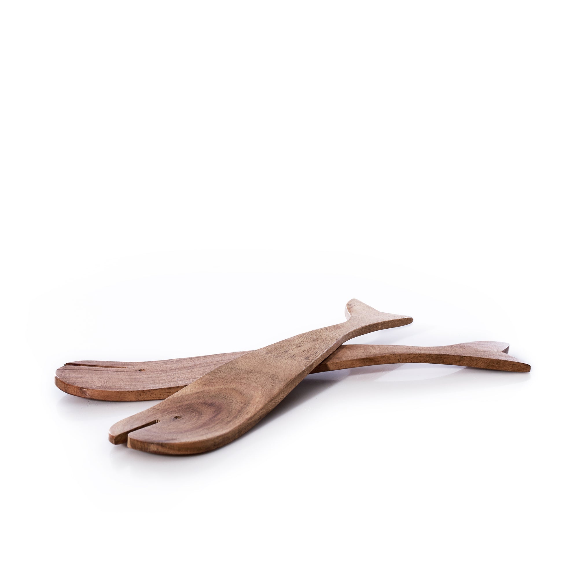 The Salad Server Set - Wood Whales by Batela USA Inc features two wooden whale-shaped servers with a natural finish, crossed and displayed on a white background to bring subtle coastal charm to your dining table. by Sea Bags