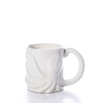 The White Octopus Mug by Batela USA Inc is a white ceramic mug with a raised octopus design, featuring one tentacle as the handle, and is shown against a plain white background. by Sea Bags