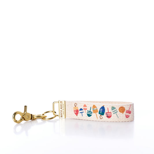 The Rustic Marlin Keychain - Downeast Buoys by Rustic Marlin features playful buoy illustrations on fabric with a gold metal clasp and ring, making it a charming canvas bag accessory that adds a whimsical, nautical touch to your everyday style. by Sea Bags