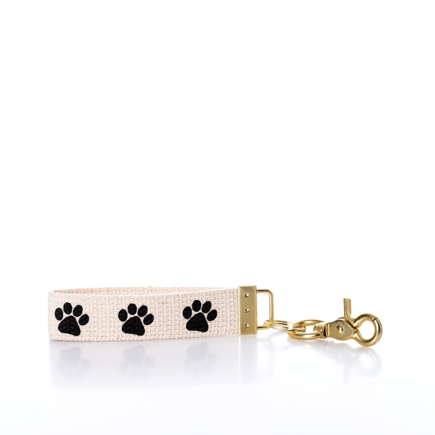 The Rustic Marlin - Keychain Paw Prints by Rustic Marlin is a beige fabric keychain featuring three black paw prints and gold metal hardware with a brass lobster clasp, perfect as a charming bag charm. Shown on a white background. by Sea Bags