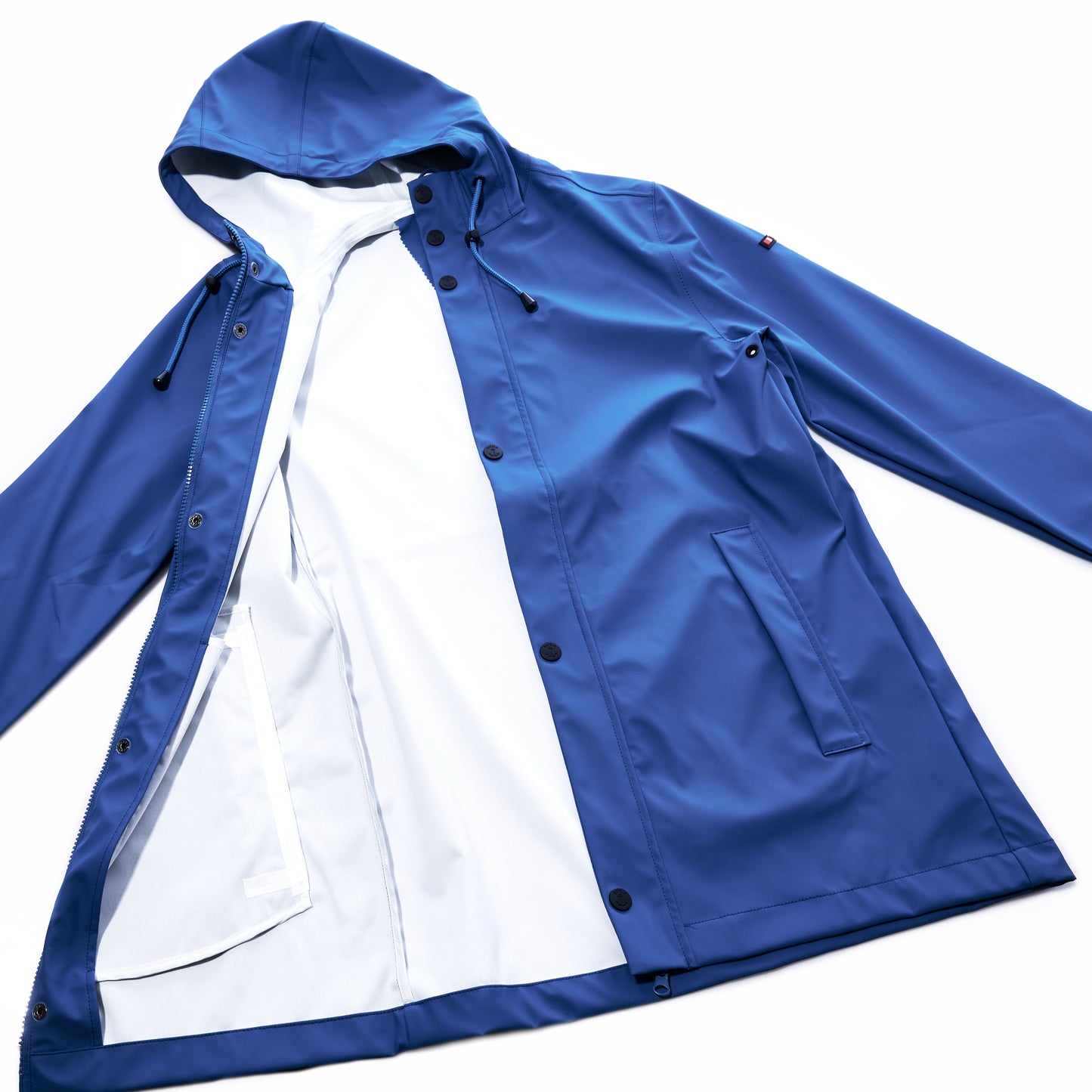 The Harborside Waterproof Raincoat - High Tide by Batela USA Inc is a blue hooded raincoat with black buttons and two front pockets, boasting a waterproof shell ideal for coastal adventures. Displayed open to reveal its white interior lining, the raincoat is laid flat on a white background. by Sea Bags