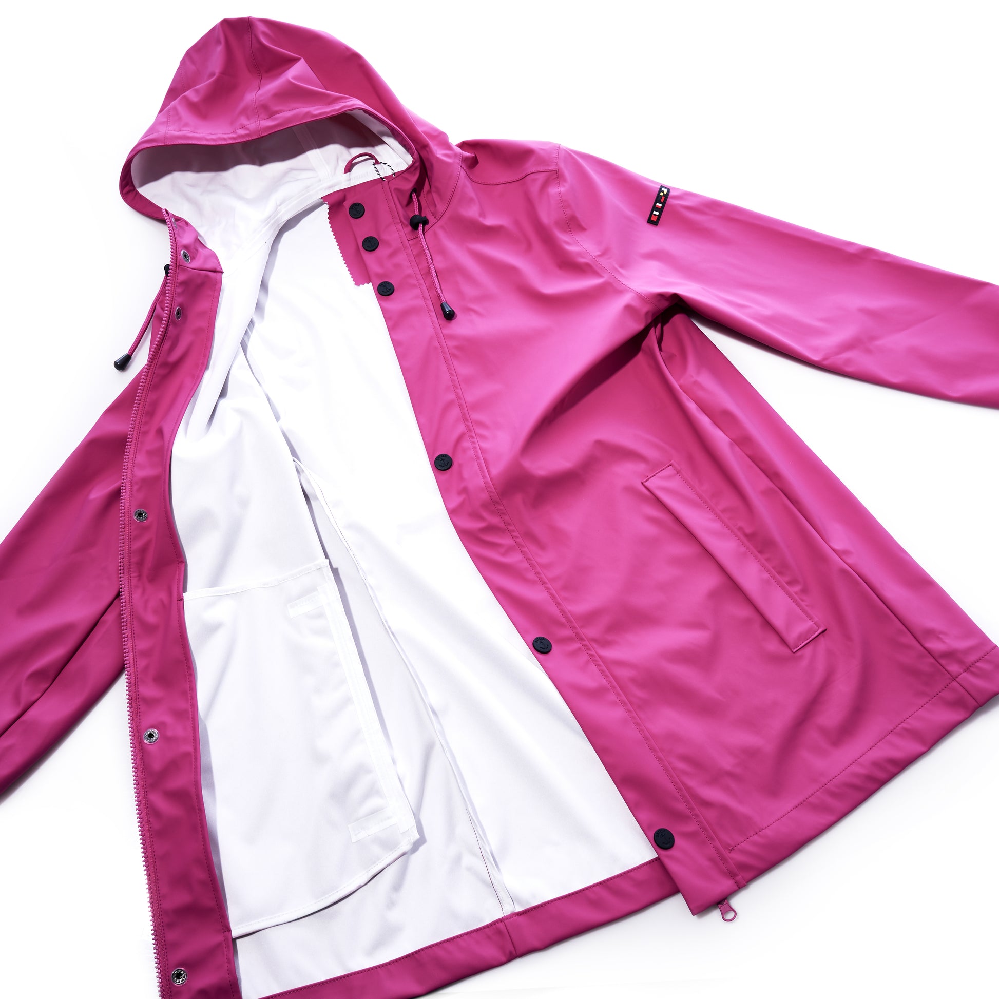 The Harborside Waterproof Raincoat in Fuchsia by Batela USA Inc is laid flat and open, showcasing its white inner lining and interior pockets. With black buttons and a hooded design, its the ideal waterproof shell for coastal adventures. by Sea Bags