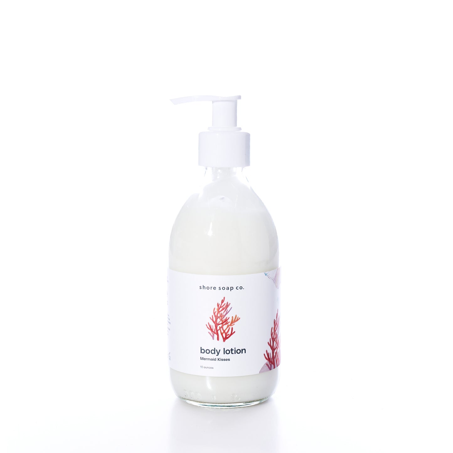 Shore Soap Co. Mermaid Kisses Eco-Friendly Body Lotion in a clear glass pump bottle with a white label featuring a red coral design, photographed on a white background. This natural body lotion provides nourishing care in an elegantly designed, eco-friendly package. by Sea Bags