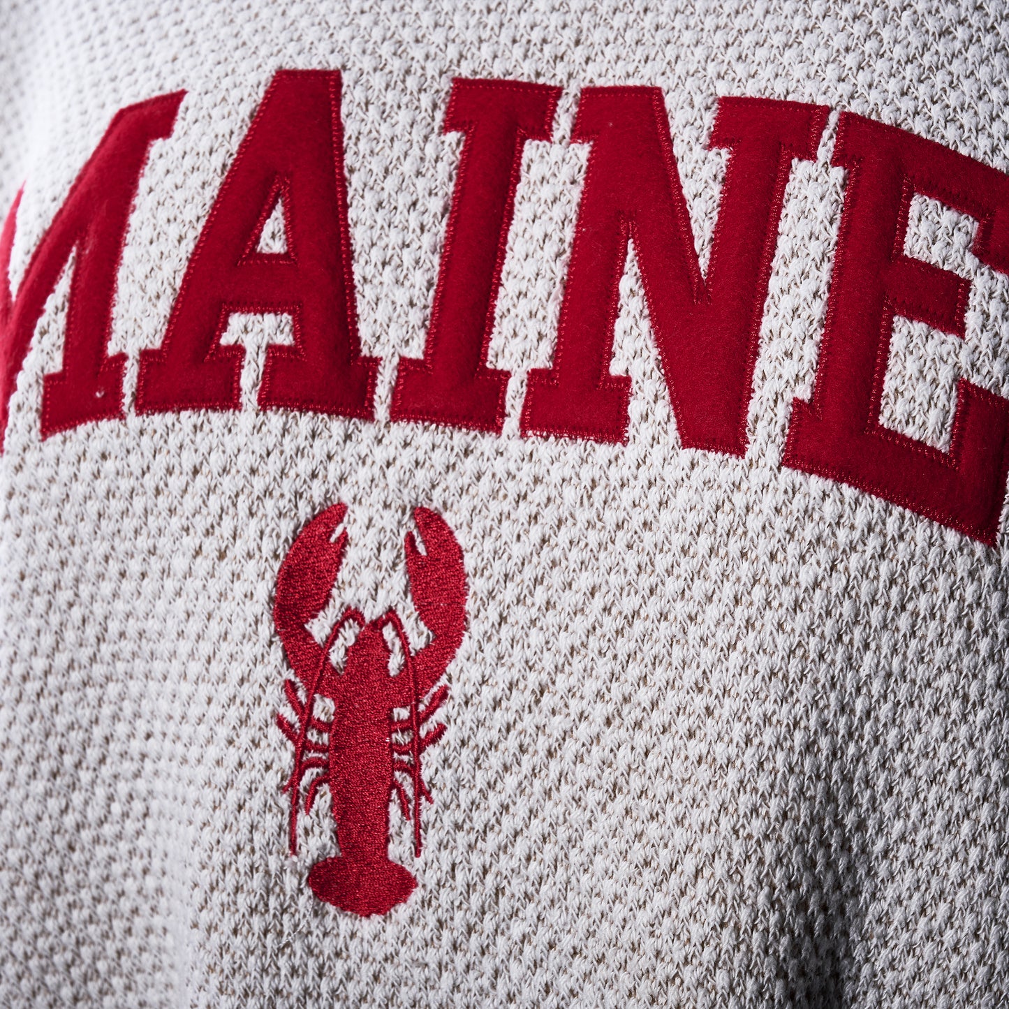 A close-up of the Soft As A Grape Popcorn Fleece Pullover in Oatmeal - Maine Lobster, showcasing its textured white fabric with “MAINE” embroidered in red letters above a red lobster graphic—a tribute to Maine’s lobster tradition and coastal heritage.
