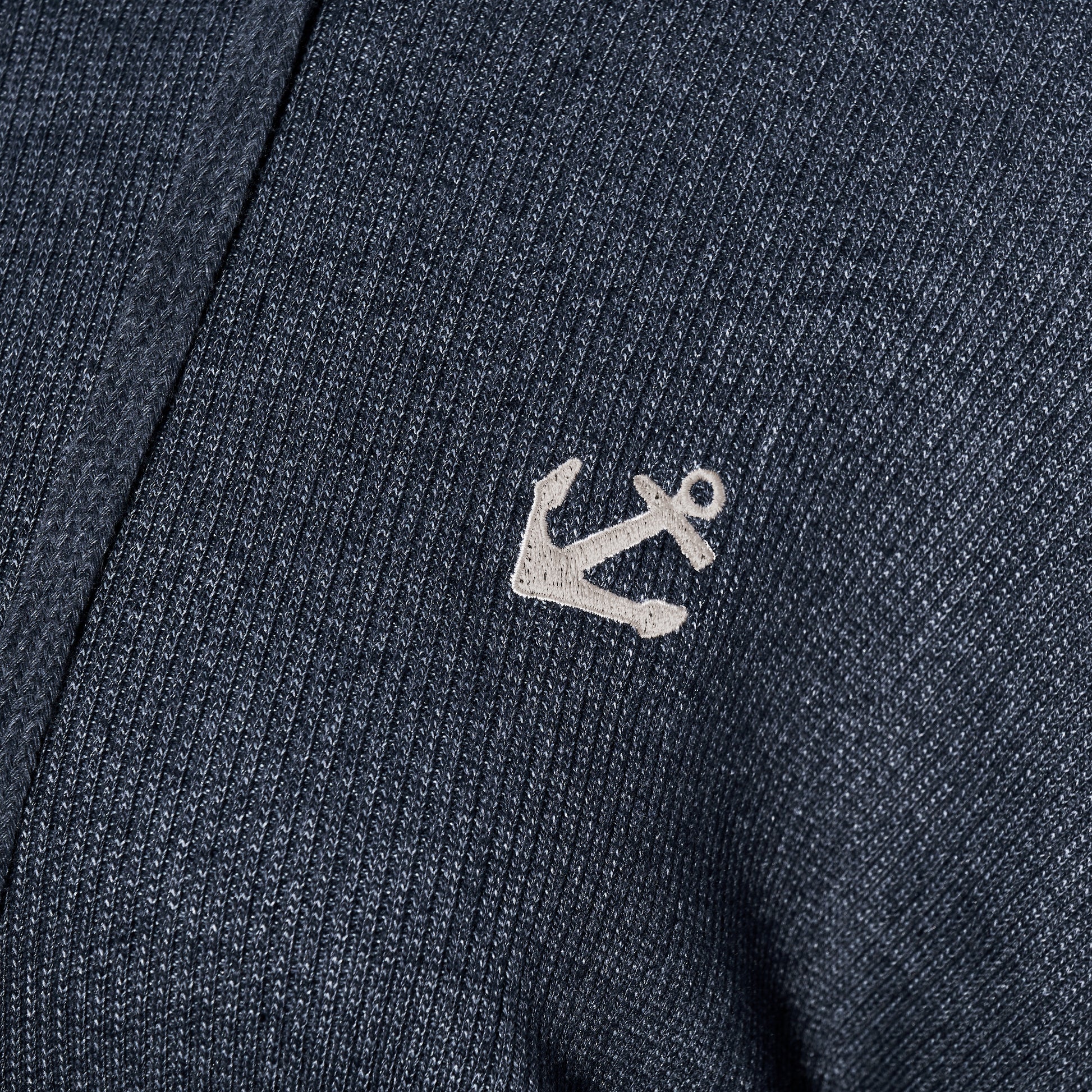 Close-up of the Soft As A Grape Ribbed Hoodie Pullover - Navy Anchor, showcasing its navy blue ribbed fabric and a small white embroidered anchor, perfect for bringing a subtle coastal style to your look. by Sea Bags