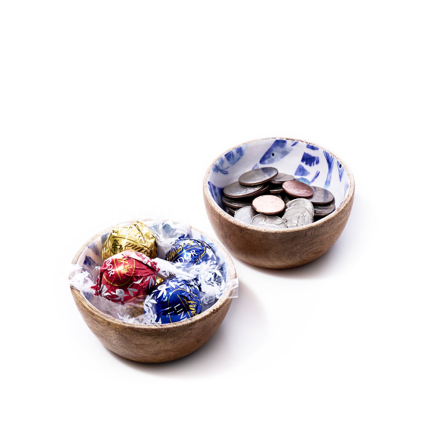 Two small bowls: the first, Batela USA Incs Enameled Wood Bowl - Striped Fish, features an enameled mango wood finish with a delicate striped fish design and holds assorted wrapped chocolates; the second contains various coins. Both bowls are displayed on a white background. by Sea Bags