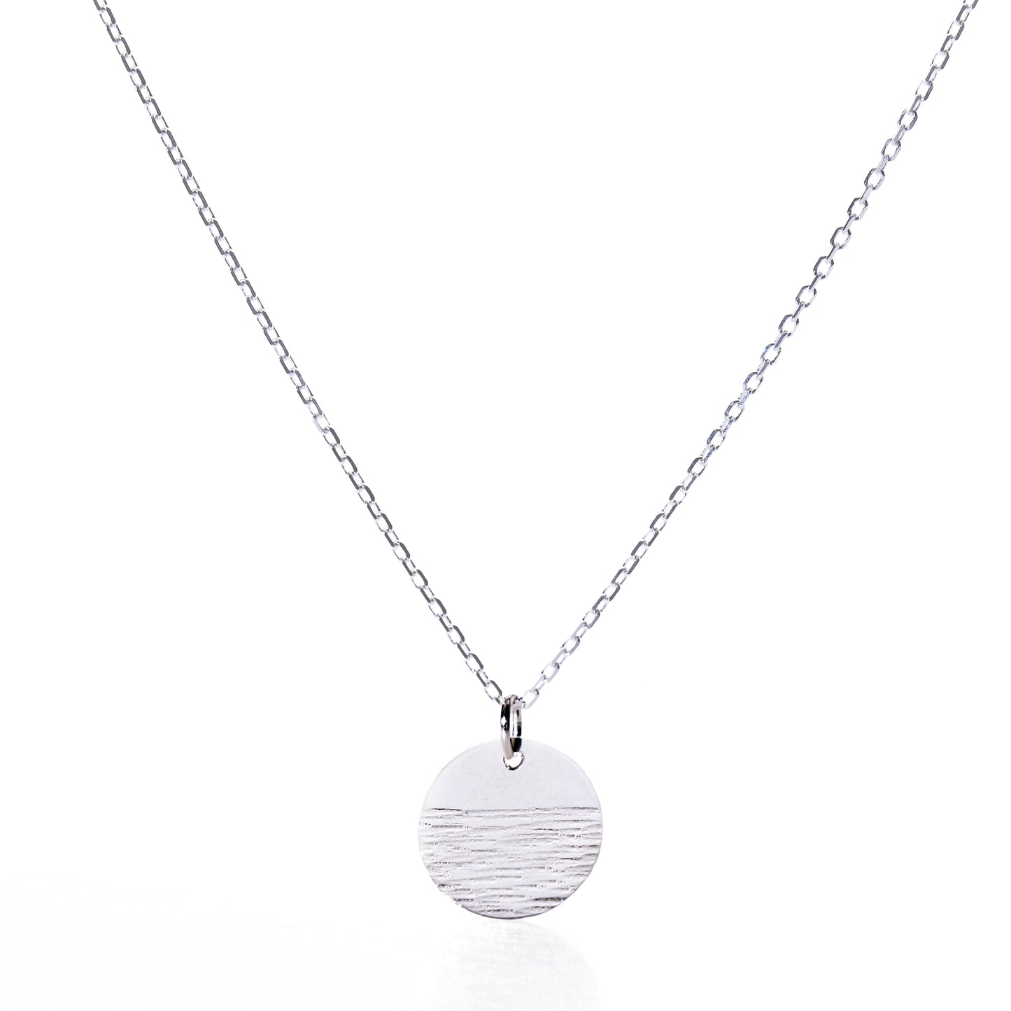 Elevate your jewelry collection with the Pendant Necklace - Horizon Silver by Maine Yoga Jewelry: a refined silver chain showcasing a round, textured silver pendant accented with a distinctive horizontal line detail, beautifully presented against a white background. by Sea Bags