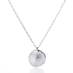 Pendant Necklace - Sand Dollar Silver by Maine Yoga Jewelry features a silver chain necklace with a textured, round sand dollar-inspired pendant, crafted sustainably and evoking the coastal beauty of Maine, shown against a white background. by Sea Bags