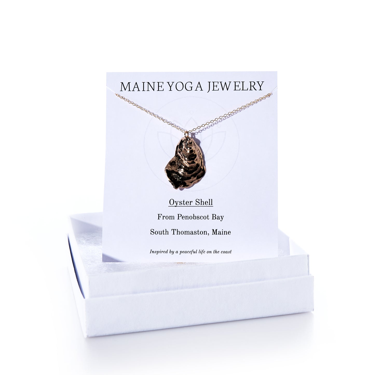 A Pendant Necklace - Large Oyster Bronze from Maine Yoga Jewelry, featured as part of our coastal jewelry collection, is displayed on a branded card and rests atop a white jewelry box. by Sea Bags