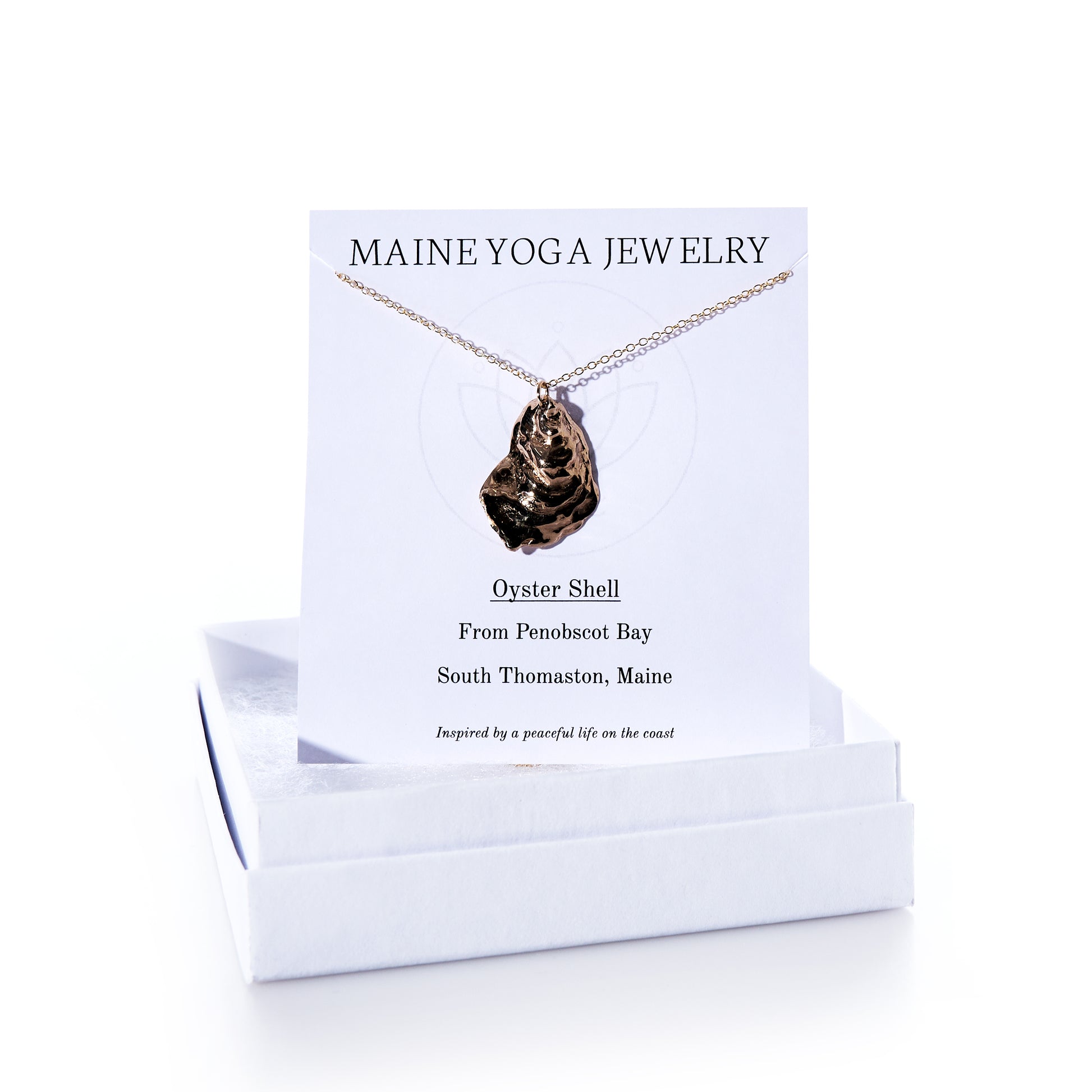 A Pendant Necklace - Large Oyster Bronze from Maine Yoga Jewelry, featured as part of our coastal jewelry collection, is displayed on a branded card and rests atop a white jewelry box. by Sea Bags