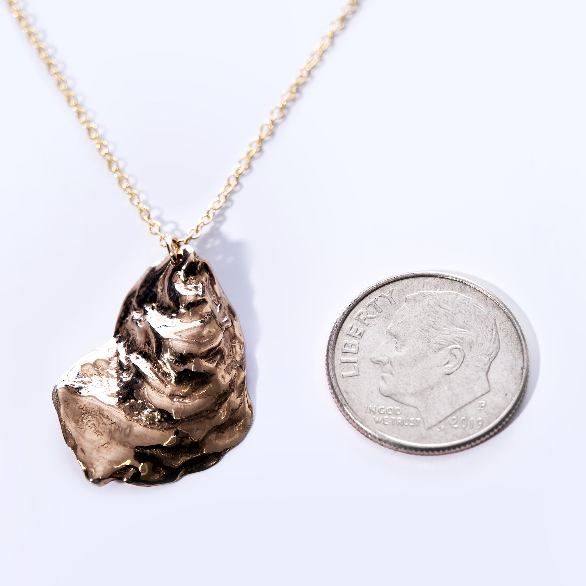 Pendant Necklace - Large Oyster Bronze by Maine Yoga Jewelry on a fine chain, shown beside a U.S. dime for size reference and displayed against a light background—this piece captures the laid-back sophistication of coastal jewelry, ideal for bringing seaside charm to your collection. by Sea Bags