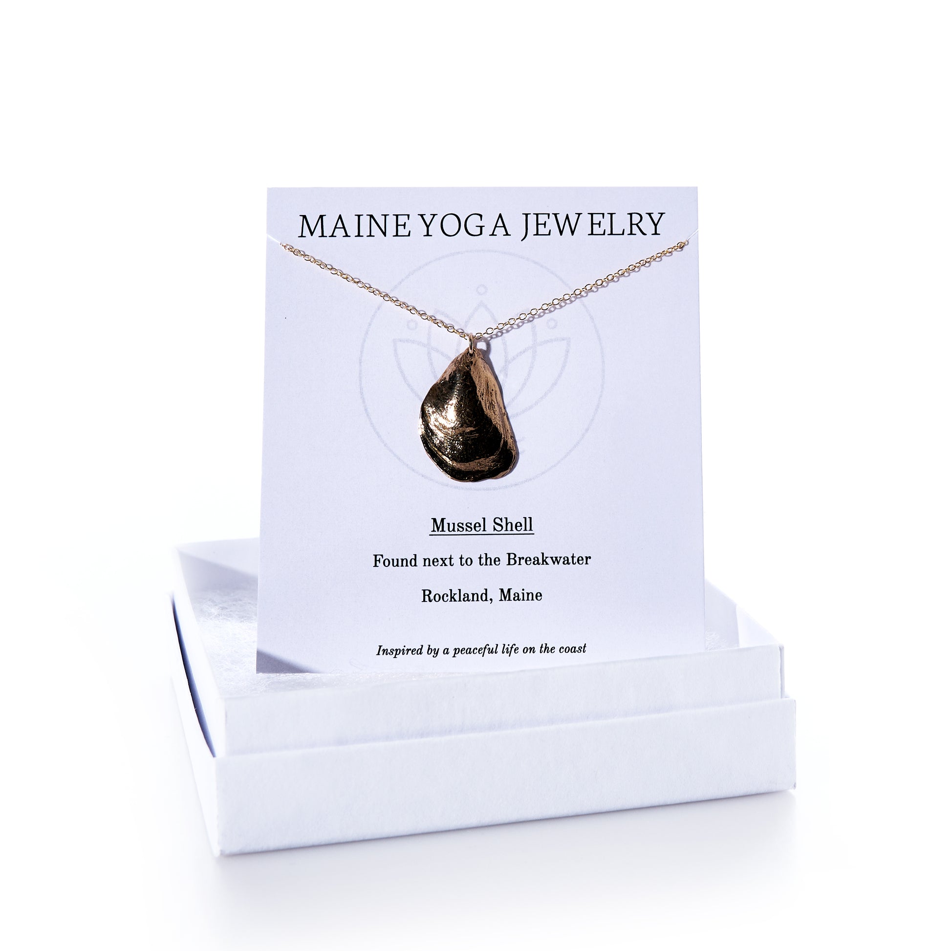 Pendant Necklace - Large Mussel Bronze displayed on a card labeled Maine Yoga Jewelry with descriptive text, set atop a white jewelry box. This elegant piece of coastal jewelry features a beautifully crafted large bronze mussel pendant—perfect for those who treasure seaside memories. by Sea Bags