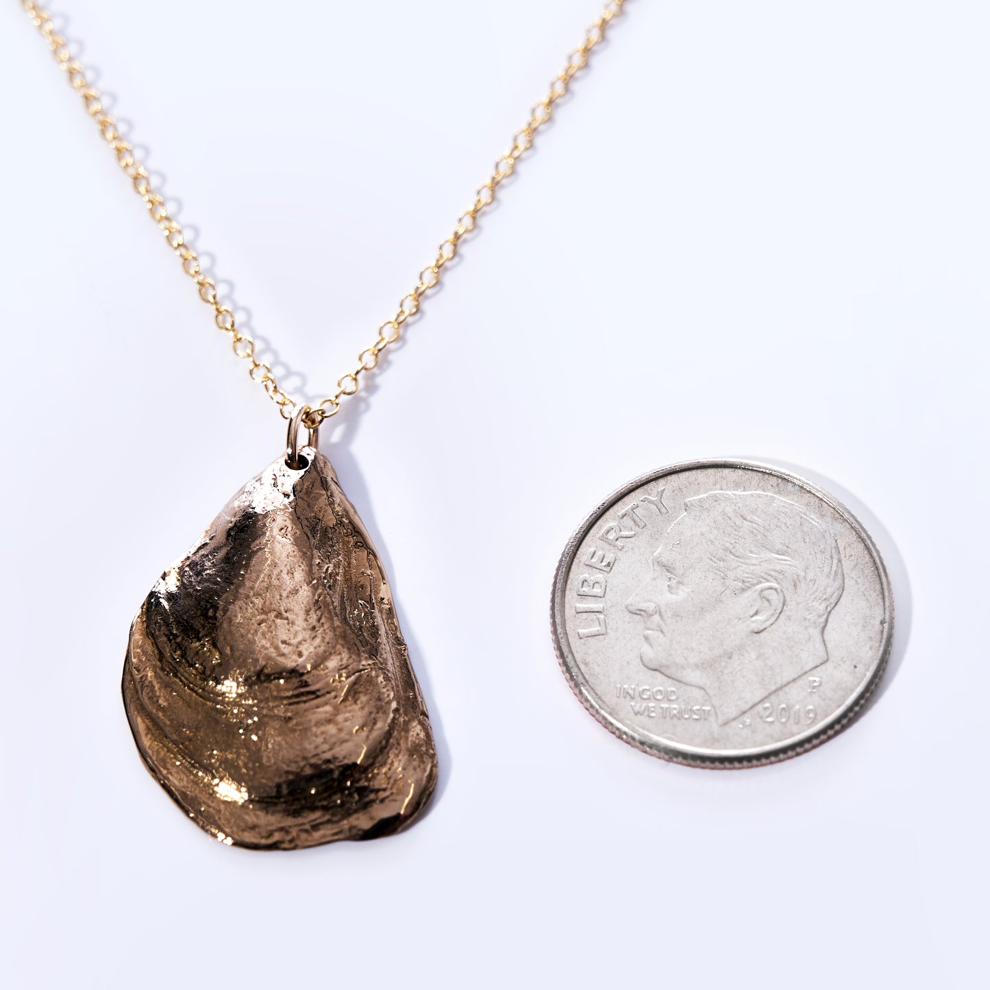 A Large Mussel Bronze Pendant Necklace by Maine Yoga Jewelry, ideal for coastal jewelry lovers, is displayed next to a dime for scale on a white background. by Sea Bags