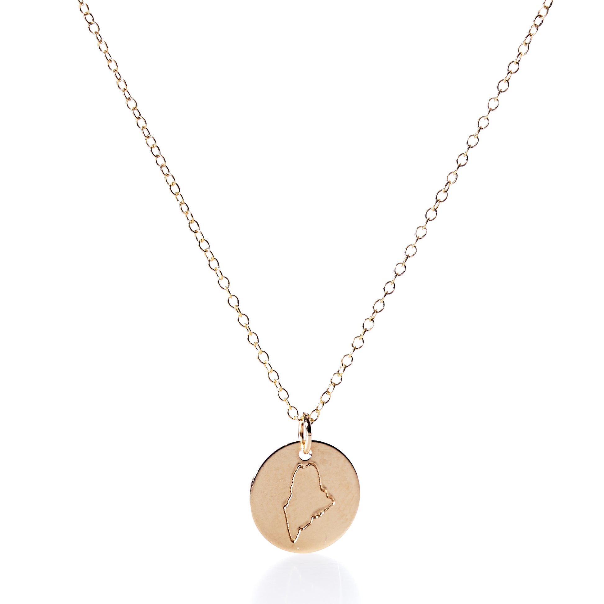 Pendant Necklace - Gold Maine by Maine Yoga Jewelry features a round gold charm engraved with the outline of Maine, artfully displayed on a plain white background. Expertly crafted in Maine, this piece showcases timeless elegance and distinctive craftsmanship. by Sea Bags