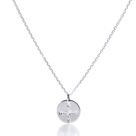 Discover the Pendant Necklace - Silver Compass Rose by Maine Yoga Jewelry, featuring a round silver pendant engraved with a compass rose showing N, S, E, and W directions. This nautical necklace is displayed on a simple chain against a white background and is proudly made in Maine. by Sea Bags