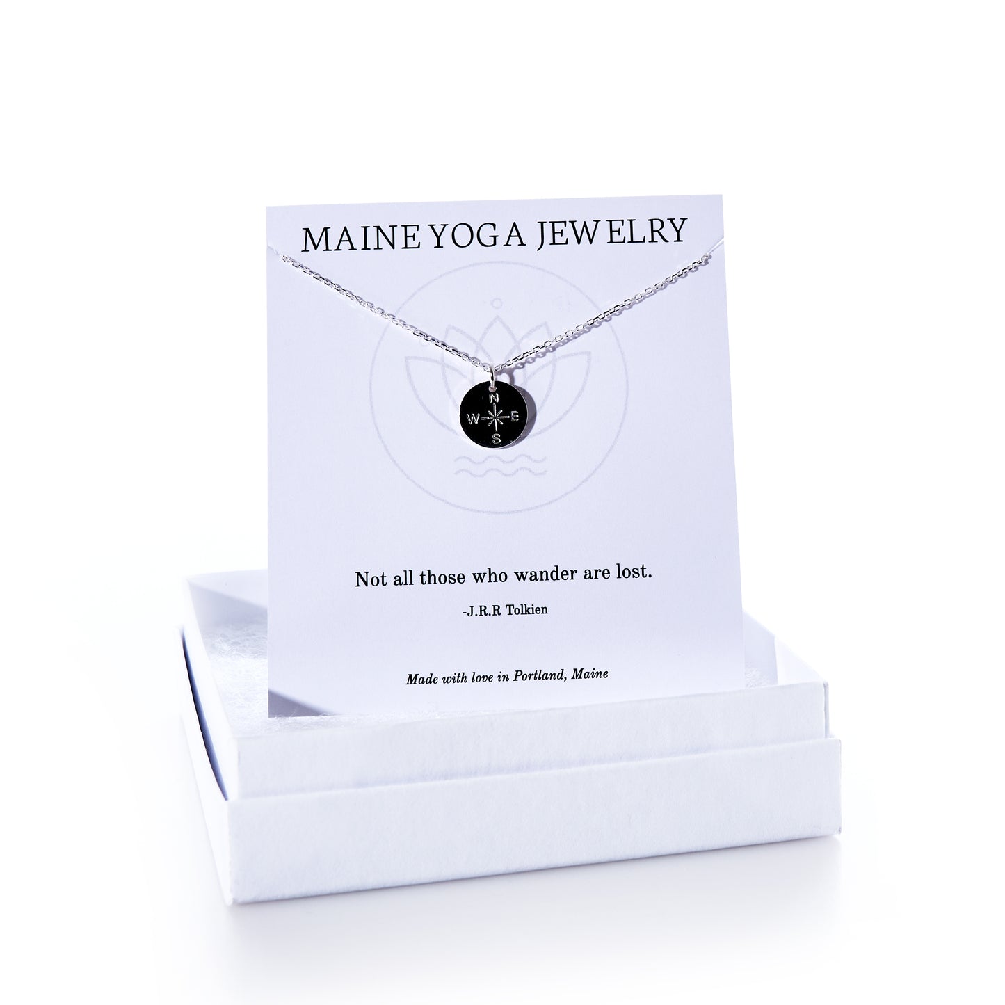 A Pendant Necklace - Silver Compass Rose by Maine Yoga Jewelry features a round compass rose pendant and is beautifully presented on a white card inscribed with the brand name and a J.R.R. Tolkien quote, all nestled inside a white jewelry box. Crafted with care in Maine, this elegant necklace embodies timeless coastal charm. by Sea Bags