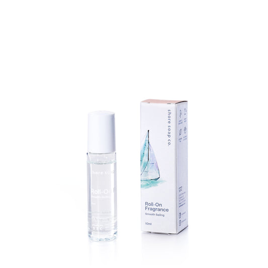 A small bottle of true’s Smooth Sailing Eco-Friendly Roll-On Fragrance, made with clean fragrance oils, stands next to its branded box adorned with a sailboat illustration. This portable perfume is ideal for freshening up while on the go.