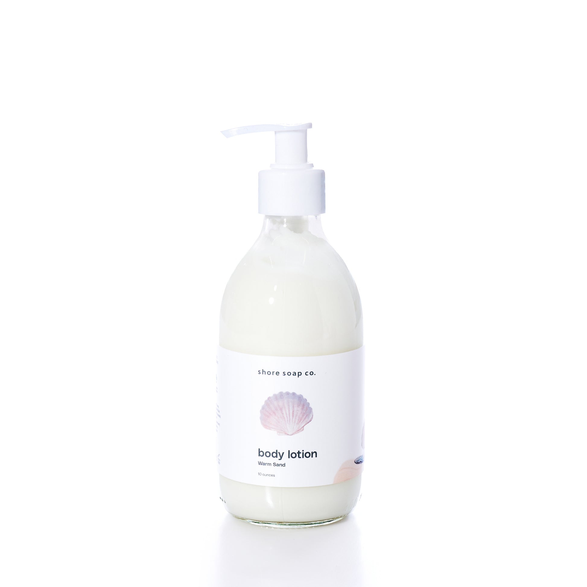 A clear pump bottle of true Warm Sand Eco-Friendly Body Lotion with a white label featuring a seashell graphic, photographed on a white background. Formulated with natural oils to help hydrate dry skin, this lotion provides nourishment while supporting sustainability.