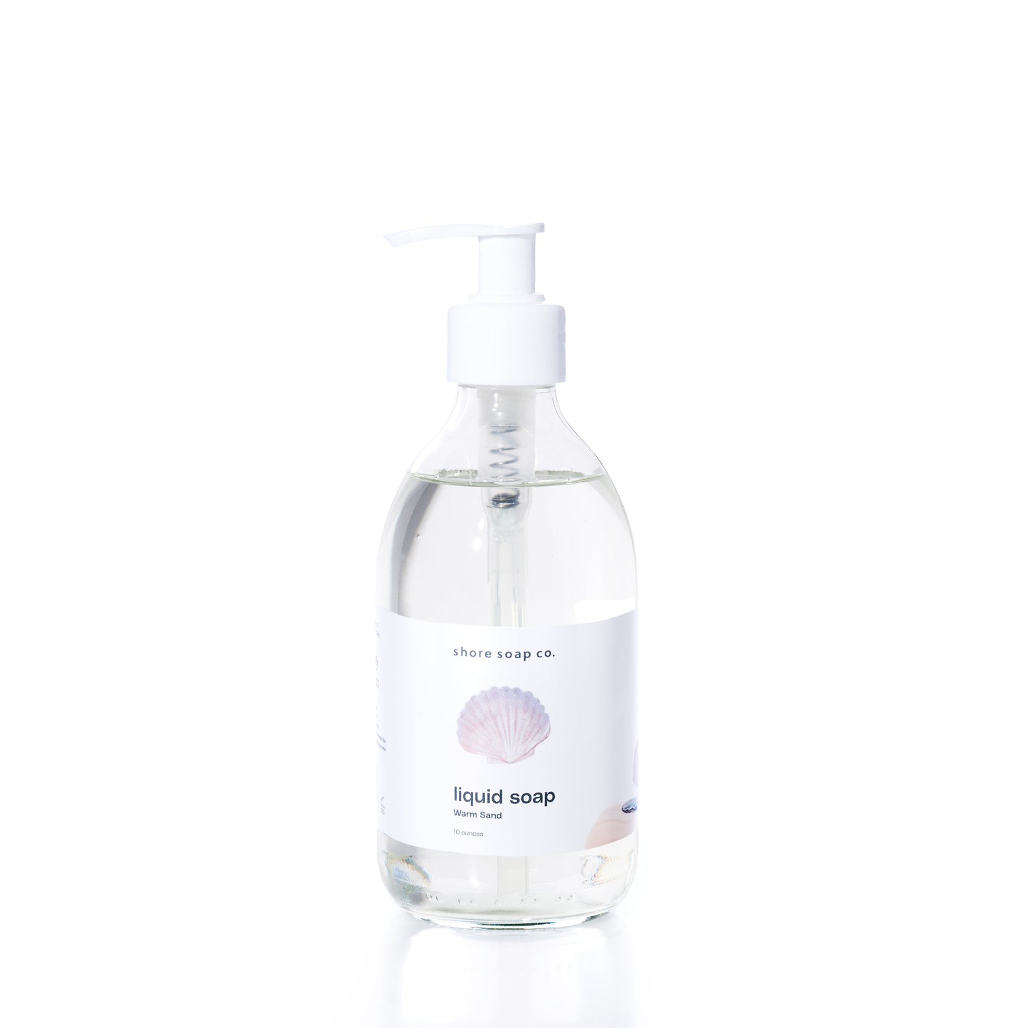 Clear pump bottle of Warm Sand Eco-Friendly Liquid Soap by Shore Soap Co., featuring a white label with a seashell graphic and “ocean scent” text, set against a plain white background. This gentle, pH-balanced formula is crafted to cleanse without harsh ingredients.