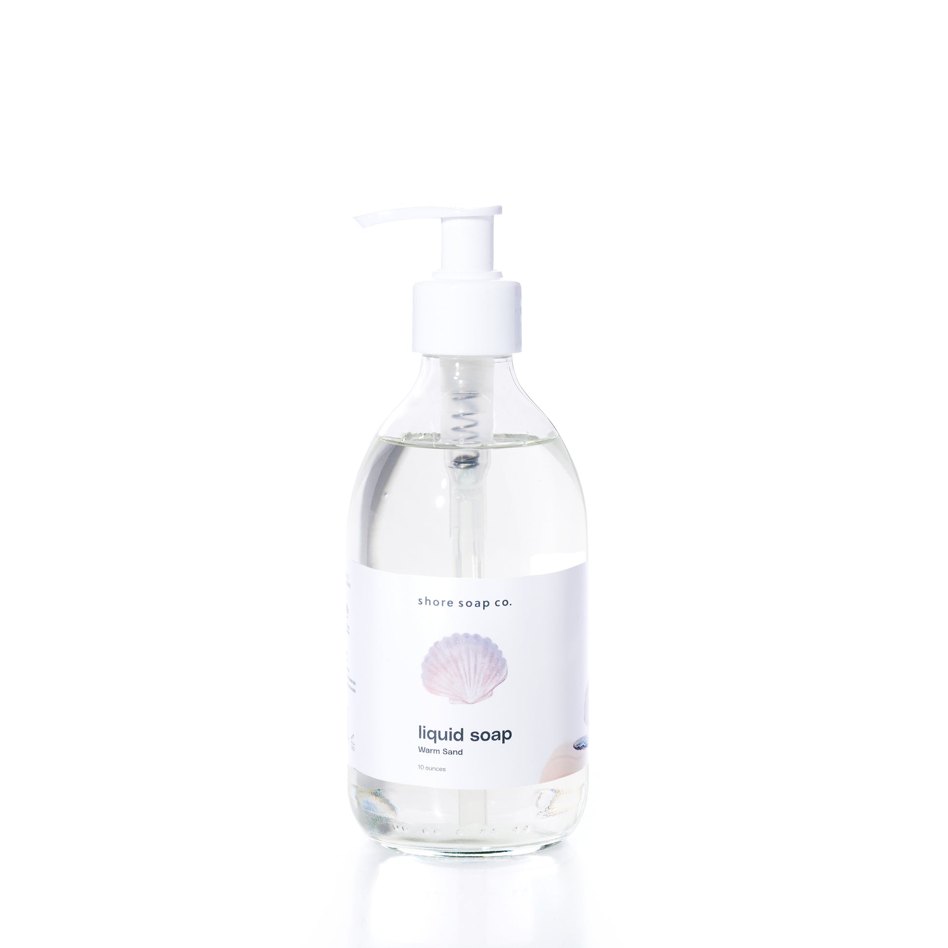 Clear pump bottle of Warm Sand Eco-Friendly Liquid Soap by Shore Soap Co., featuring a white label with a seashell graphic and “ocean scent” text, set against a plain white background. This gentle, pH-balanced formula is crafted to cleanse without harsh ingredients.