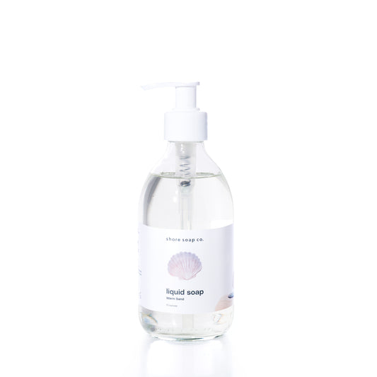 Clear pump bottle of Warm Sand Eco-Friendly Liquid Soap by Shore Soap Co., featuring a white label with a seashell graphic and “ocean scent” text, set against a plain white background. This gentle, pH-balanced formula is crafted to cleanse without harsh ingredients.