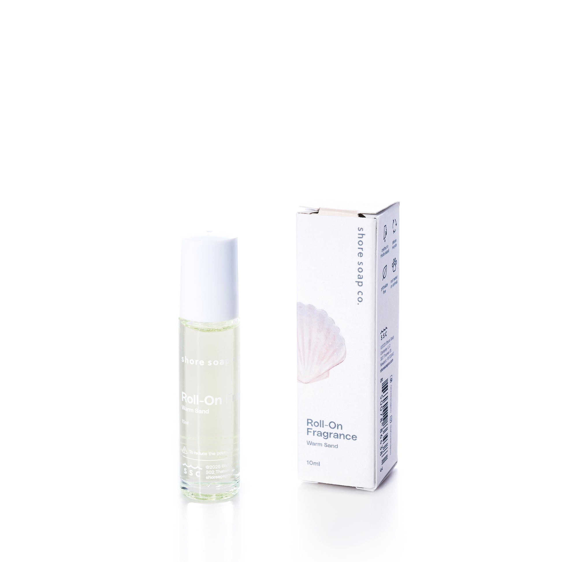 A roll-on fragrance bottle stands beside its box, labeled “Shore Soap Co. Warm Sand Eco-Friendly Roll-On Fragrance, 10ml,” featuring a seashell graphic on the packaging. This alcohol-free roll-on fragrance provides a refreshing and convenient way to experience your favorite scent wherever you go. by Sea Bags