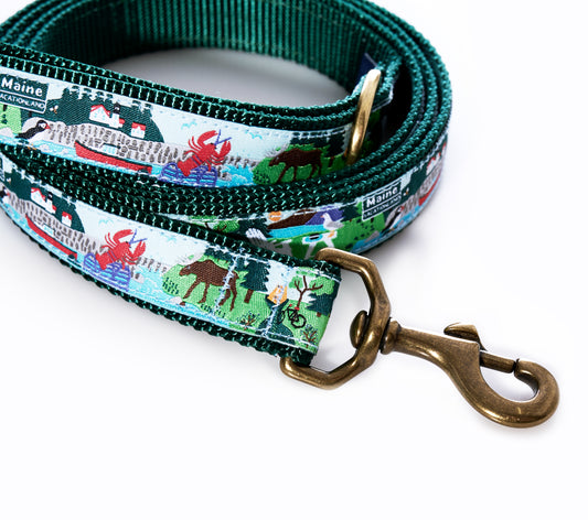 The Vacationland Dog Leash by Belted Cow features a green and white Maine-themed design on heavy-duty nylon, decorated with illustrated dogs, people, and trees, and finished with a brass clasp and an L.L.Bean Maine label. by Sea Bags