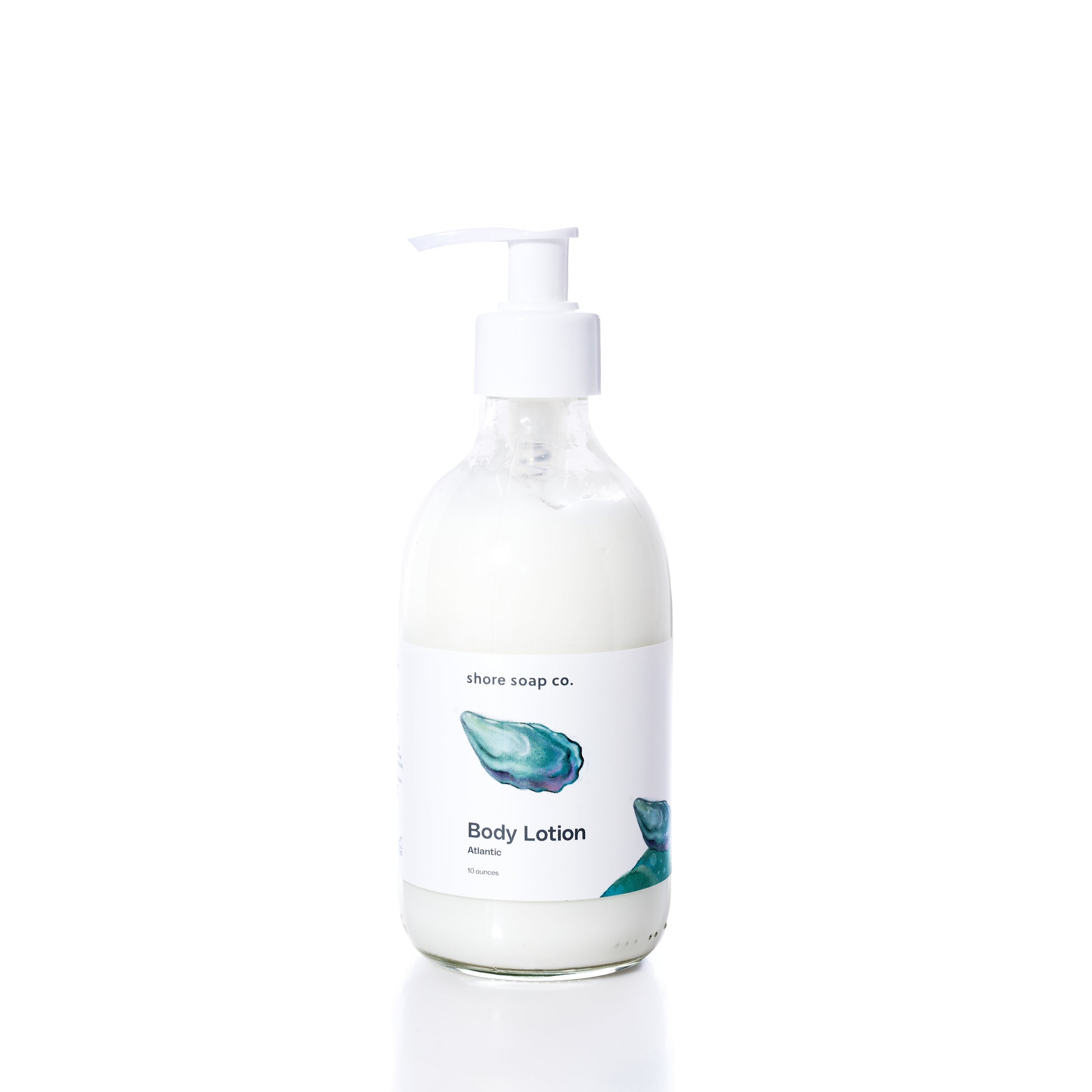A clear pump bottle labeled “Shore Soap Co. Atlantic Eco-Friendly Body Lotion” with an illustrated blue oyster shell, filled with white lotion, set against a plain white background. This moisturizer for sensitive skin is made with natural ingredients for gentle, nourishing care. by Sea Bags