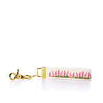 Introducing the Rustic Marlin Keychain - Pink Lupine by Rustic Marlin: a white canvas keychain with a gold clasp, adorned with a lovely pink and green lupine-inspired floral pattern—a charming New England souvenir for any collection. by Sea Bags